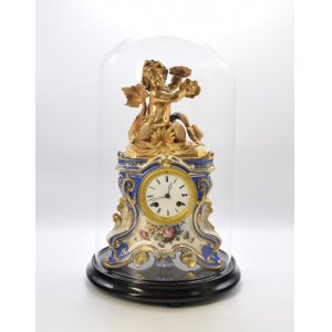 Clock in a porcelain case, with a tritone - bronze setting (under a glass shade)