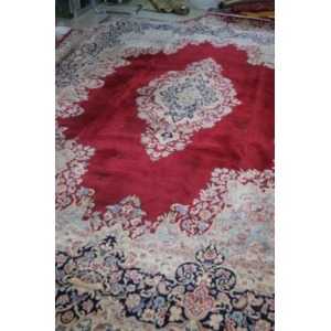 Très grand tapis Kirman en laine. Décor de végétaux sur fond rouge. Porte une signature. 440x300 cm