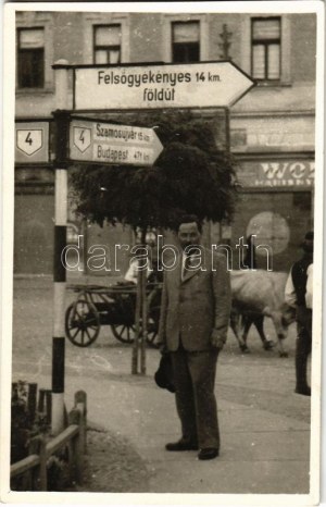 ~1940 Dés, Dej; utcakép, férfi kalappal az útjelző tábla alatt, mögötte ökrös szekér / street view, man with hat...